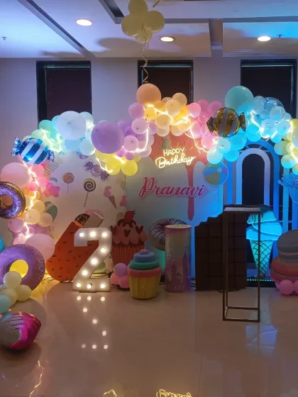 A sweet and delightful candy theme decoration for a second birthday. This setup features pastel-colored balloons, large candy and ice cream props, a neon "Happy Birthday" sign, and a light-up number "2".