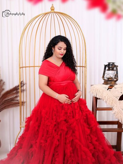 A beautiful solo portrait of a mother-to-be in a red ruffled gown, seated in our bohemian-themed studio setup.