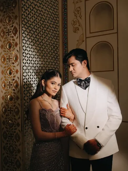 A classic portrait from a sangeet night, exuding old-world charm and elegance. The groom in his white tuxedo and the bride in her lavender gown create a picture-perfect moment against the ornate palace interior.