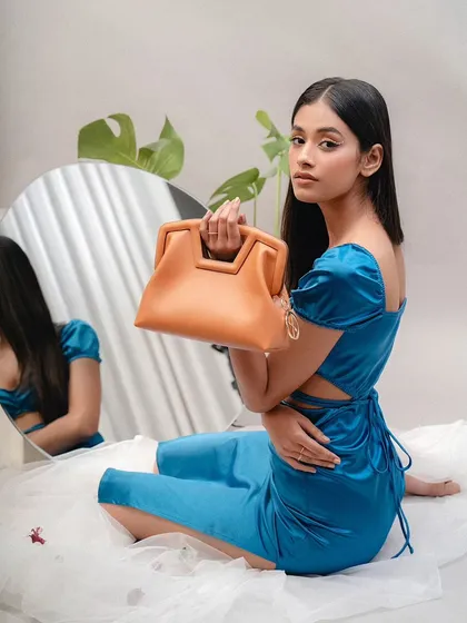 A full-length studio shot for Sarjaa, with the model seated. The use of a mirror and flowing fabric creates an artistic and elegant setting for the handbag.