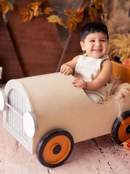 A close-up of a smiling baby in his toy car. His happy expression is the highlight of this adorable, woodland-themed portrait.