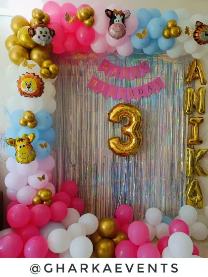 A jungle-themed birthday with a mix of animal characters. The silver tinsel backdrop is framed by a colorful balloon arch featuring foil animal heads and the birthday girl's name in gold letters.