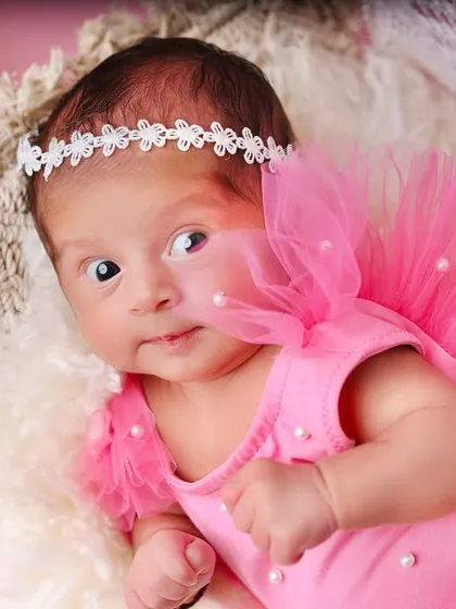 An alert newborn in a sweet pink outfit with tulle sleeves, looking directly at the camera with her big, beautiful eyes.