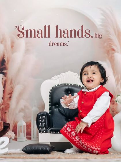 A happy moment from a first birthday studio session. The child's bright red dress stands out beautifully against the soft, neutral tones of the boho backdrop.