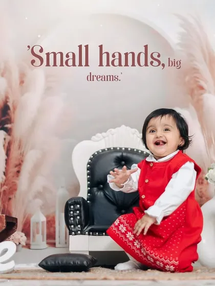A happy moment from a first birthday studio session. The child's bright red dress stands out beautifully against the soft, neutral tones of the boho backdrop.