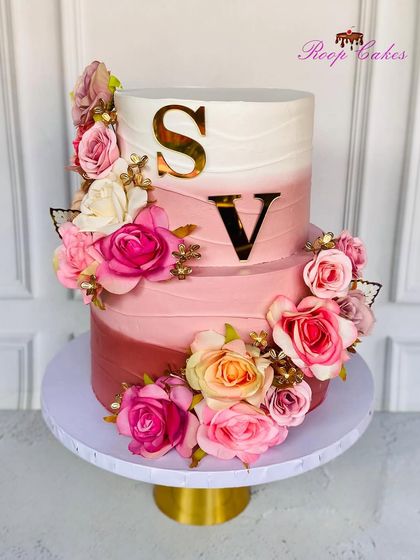 A beautiful two-tier cake in shades of pink, perfect for an engagement or anniversary. The cake is adorned with a cascade of roses and personalized with the couple's initials in gold.