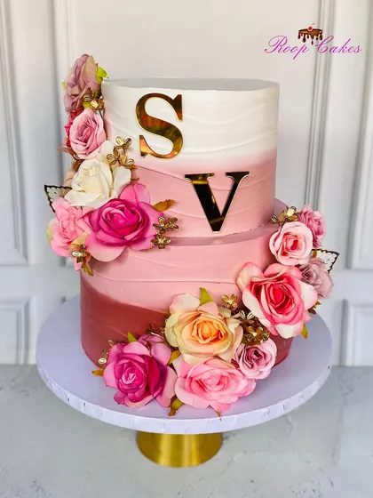 A beautiful two-tier cake celebrating a new chapter. This design features a soft pink ombre effect, a cascade of fresh flowers, and the couple's initials in gold for a touch of personalized elegance.