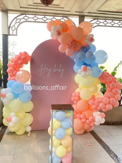 A full view of the 'Hey Baby' setup, including the pink arched backdrop, balloon garland, and a plinth for the cake.