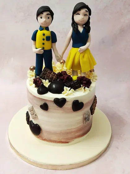 This couple anniversary cake celebrates a personal love story, with custom figurines and a base decorated with chocolate hearts.