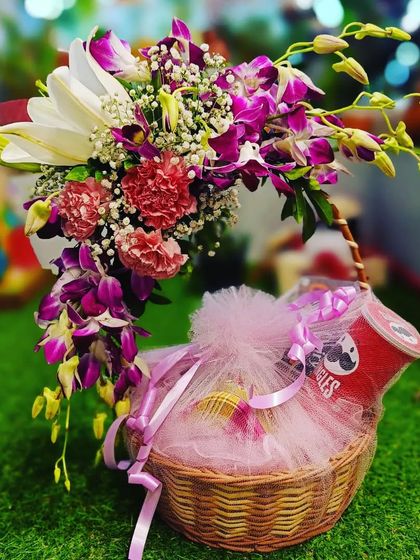 This charming basket hamper combines goodies with a beautiful fresh flower arrangement. The cascading orchids and lilies add a touch of luxury to the gift of Pringles and other treats.