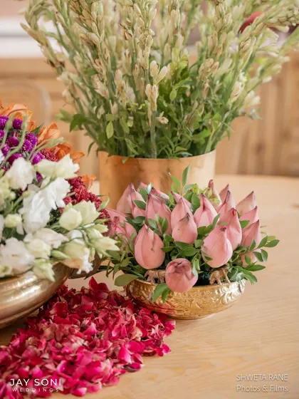 A close-up on a table centerpiece, highlighting the beautiful pink lotus buds and a trail of scattered red rose petals.