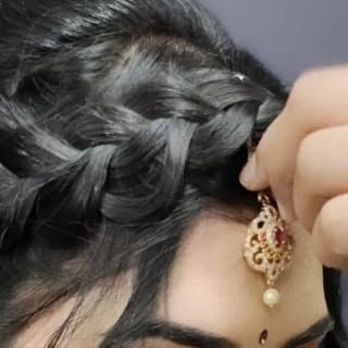 A close-up of a student creating a braided hairstyle and placing a maang tikka. This shows the precision and attention to detail taught in our hairstyling classes.