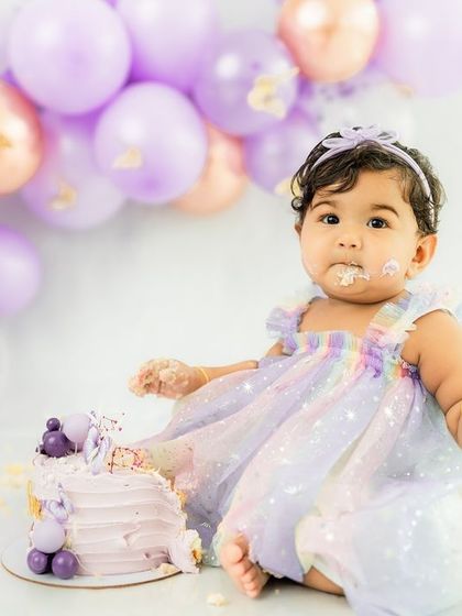 A picture of pure satisfaction. This little one is thoroughly enjoying her beautiful lavender cake, surrounded by matching balloons.