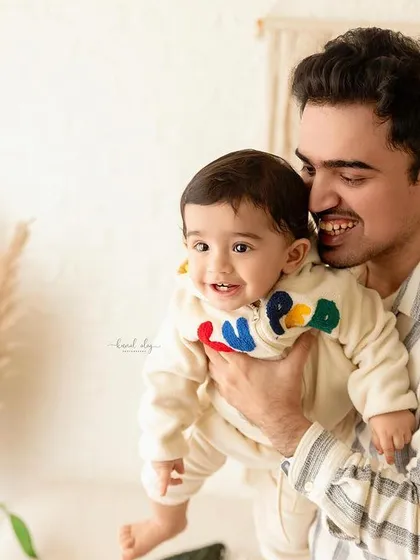 A happy father holding his son during his first birthday photoshoot. The boho studio setting provides a warm and celebratory backdrop.