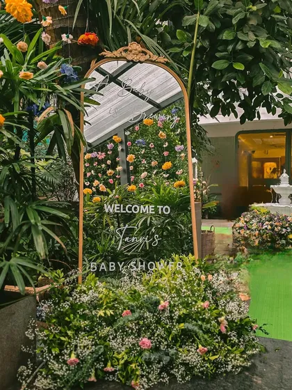 A beautiful welcome sign for a baby shower, nestled in a lush, green entranceway. The gold-framed mirror adds a touch of vintage elegance.