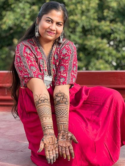 A happy client sitting on a rooftop, proudly displaying her full-arm personalized mehendi.