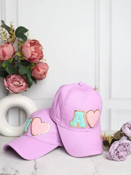 Your style, your initial. These trendy lilac baseball caps are customized with chenille initial and heart patches, making them a cute and personal accessory.