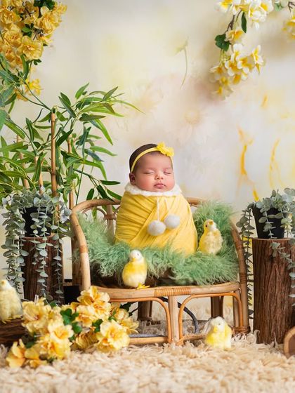 A full view of the yellow themed setup, with the baby wrapped and resting on a small bench. The background and props create a complete, cheerful scene.