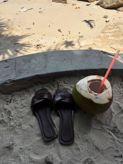 The simple pleasures of a beach vacation: sandals in the sand and fresh coconut water.