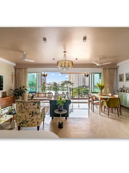 An open and vibrant living and dining area, where floral armchairs and a green chesterfield sofa create a lively, eclectic feel. The layout flows seamlessly towards a balcony, filling the space with natural light and connecting it to the outdoors.