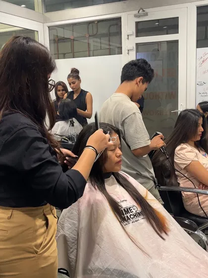 Another shot of our students practicing their haircutting and coloring skills on live models, with trainers providing guidance.