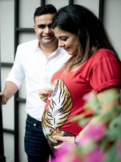 A sweet, candid moment where the couple is focused on the baby bump. The flowers in the foreground add a soft touch of color and depth to this outdoor portrait.