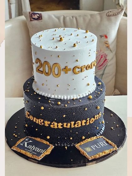A grand corporate celebration cake in black and gold, congratulating a company on achieving "200+ crores".