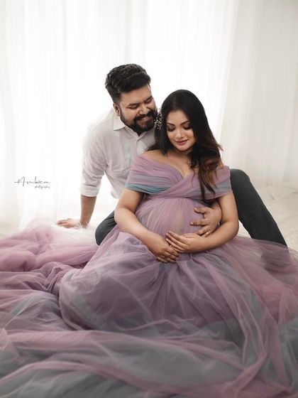 An intimate and gentle portrait. The soft lavender tulle of the gown pools around them, creating a dreamy and ethereal feel for this couple's indoor maternity photoshoot.
