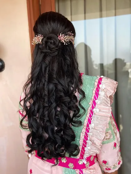A beautiful half-up rose bun with flowing curls. The floral hair accessory adds a touch of pink to match her outfit.