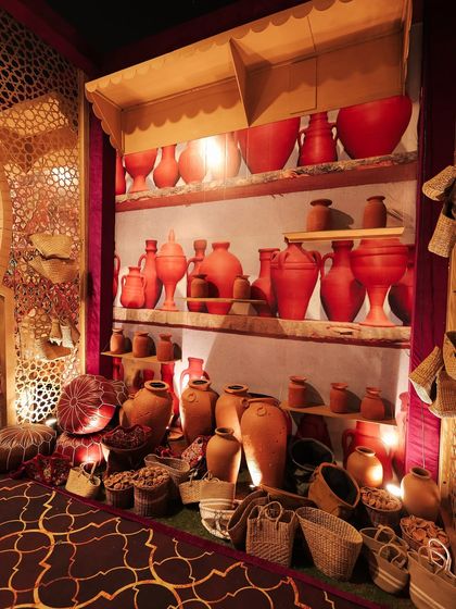 A wider view of the pottery market stall, with shelves filled with various shapes and sizes of terracotta and red-painted earthenware, creating a vibrant and artisanal display.