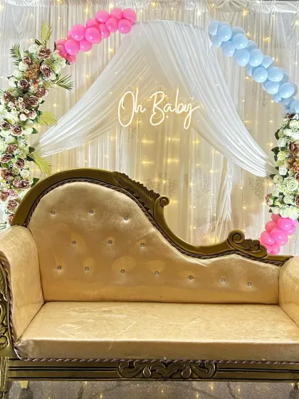 For a beautiful and functional baby shower setup, I combined a floral and balloon arch with elegant draping and a comfortable diwan for the mother-to-be. The fairy lights and "Oh Baby" neon sign add a warm, celebratory glow.