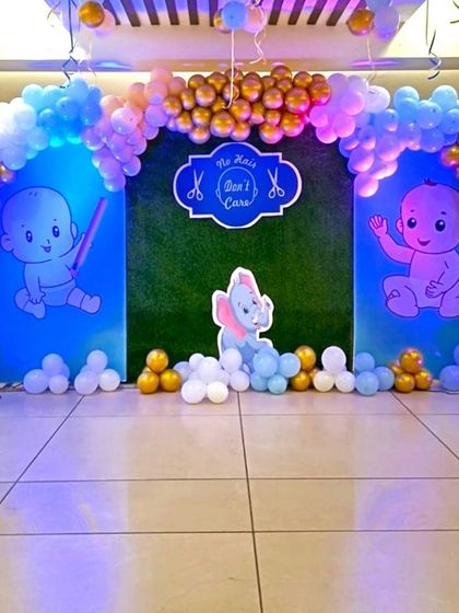 A cute balloon decoration for a Mundan (first haircut) ceremony. The backdrop features cartoon babies and an elephant, framed by a blue and gold balloon arch.