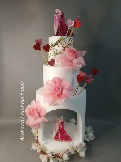 A modern and romantic anniversary cake with a unique arch structure. The design features delicate sugar flowers and couple toppers.