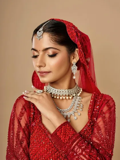 A serene bridal portrait showcasing a soft glam look with a classic red lehenga. The makeup enhances her features with gentle contouring and a neutral lip, keeping the focus on her natural beauty.