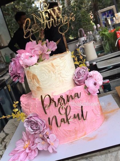 A pretty two-tier engagement cake for a new beginning. The bottom tier has a pink textured finish, while the top is a classic white with gold stenciling, all brought together with beautiful pink flowers and custom name toppers. The flavor was a crowd-pleasing white forest.
