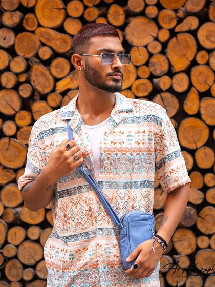 A vibrant street style shot with a textured wood background. The model's patterned shirt and accessories create a visually interesting look perfect for a fashion-forward portfolio.
