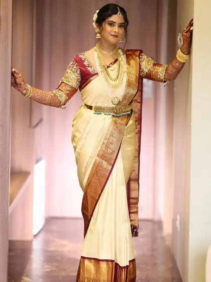 A full-length shot showcasing the bride's stunning cream and maroon silk saree and her graceful posture.