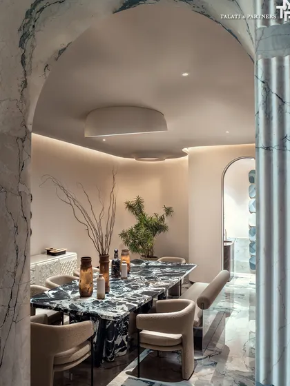 A dining space framed by a fluted marble archway, creating a sense of arrival. The design uses a bold, monolithic dining table in a dark, veined marble, which stands in beautiful contrast to the lighter tones of the surrounding architecture.