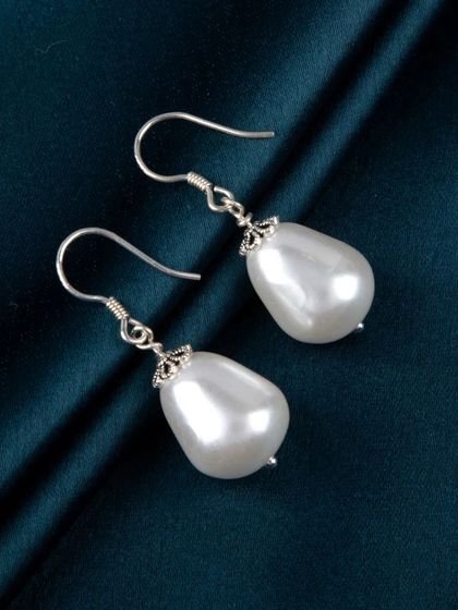 A pair of classic pearl drop earrings with silver hooks, shot against a dark, luxurious fabric.
