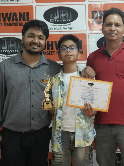 A student stands with his father and teacher, holding his certificate and trophy. We encourage family involvement in celebrating our students' artistic achievements.