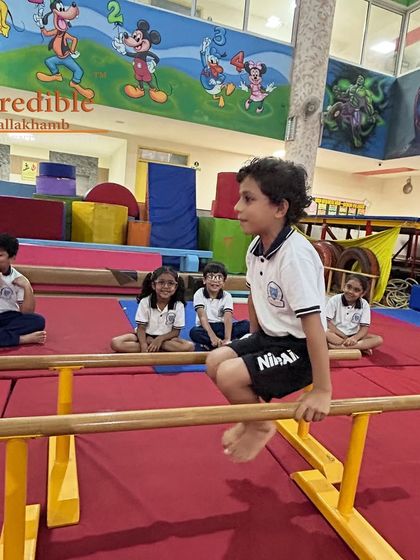 A young student holds a support position on the mini parallel bars. This exercise is fundamental for developing the arm and core strength necessary for many gymnastics skills.