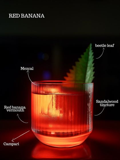 The Red Banana cocktail, a stunning creation with red banana vermouth, Campari, mezcal, and sandalwood tincture, garnished with a beetle leaf. A true sensory experience.