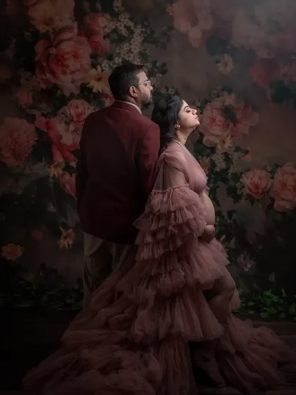 An artistic couple's portrait. Their pose is unconventional and dramatic, creating a powerful image of partnership and anticipation against a floral wall.