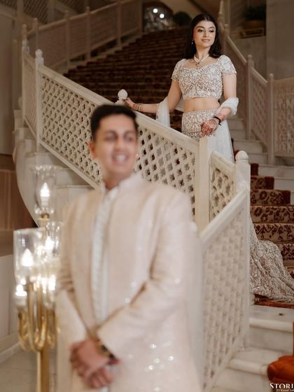 A creative portrait using depth of field, with the groom in the foreground and the bride descending a grand staircase in the background.