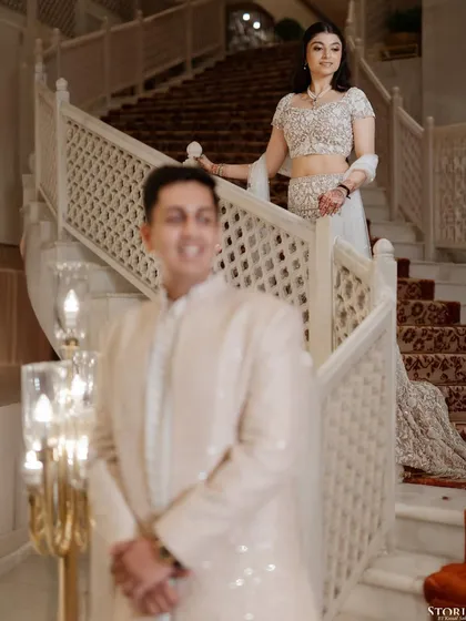 A creative portrait using depth of field, with the groom in the foreground and the bride descending a grand staircase in the background.