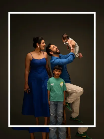 A full family portrait showing the joy and energy of a family of four. The father playfully lifts the newborn, creating a dynamic and happy scene.
