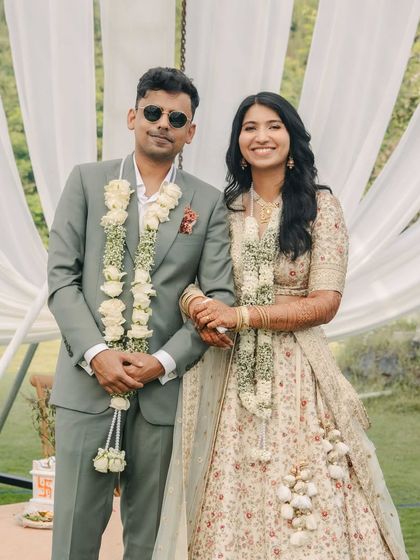 A groom and bride, perfectly coordinated. His sage green suit, tailored from a luxurious merino wool blend, was designed to complement the delicate floral accents on her lehenga.