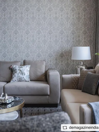 The living room of the 'Aria Residence' features a calm, neutral palette with plush sofas and a patterned wallpaper. The design focuses on creating a contemporary, elegant, and understated luxury feel.