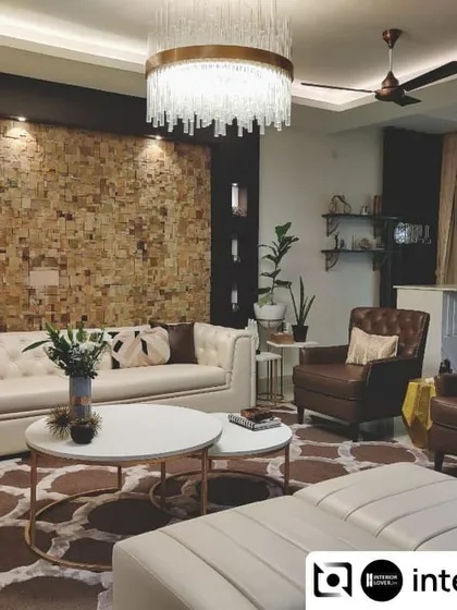 This luxurious living room features a stunning accent wall with natural stone cladding. The neutral tufted sofas, elegant chandelier, and marble coffee tables come together to create a space that is both grand and welcoming.