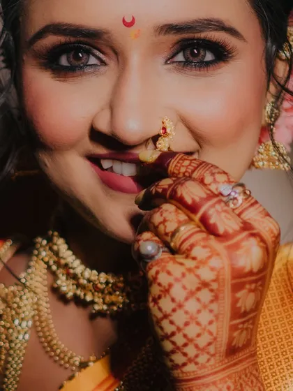 A bride's joy is radiant. This close-up portrait captures the intricate details of her henna, the sparkle in her eyes, and the traditional nath that is so central to Maharashtrian bridal beauty.